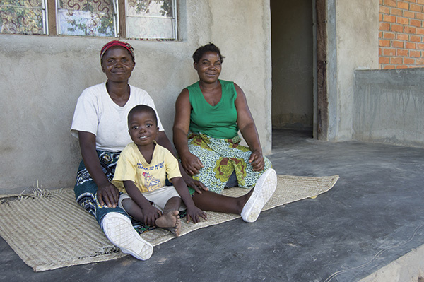 Nyirenda, her sister and grandson in front of a brick home built after the installation of the LifePump