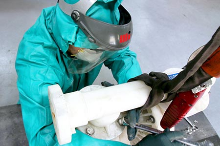 Worker in PPE disassembling an air-operated doule-diaphram (AODD) pump that is pumping hydrochloric acid