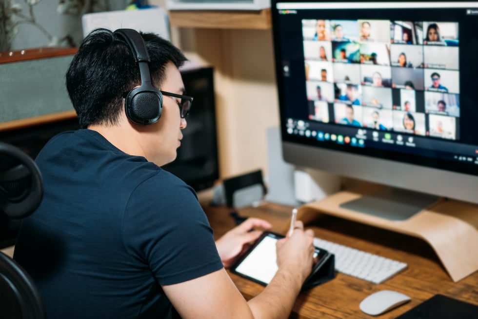 man at computer with headset looking at zoom call on screen
