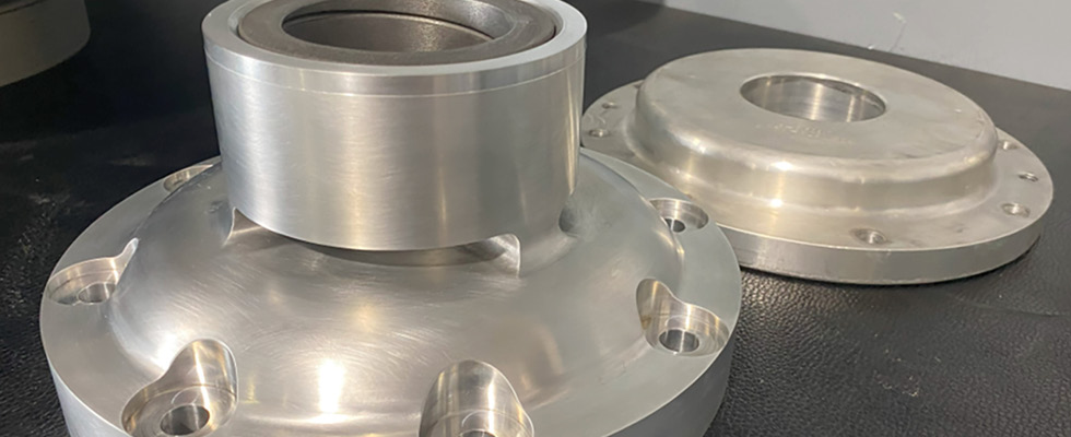 IMAGE 1: A custom housing designed for a bushing that retains the upper bearing (front) and an OEM upper bearing retainer that utilizes aluminum as a bushing material (back). (Image courtesy of Niche Cryogenic Services)