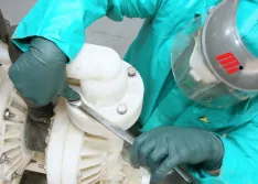 Worker in PPE disassembling an air-operated double-diaphragm (AODD) that is pumping hydrochloric acid. 